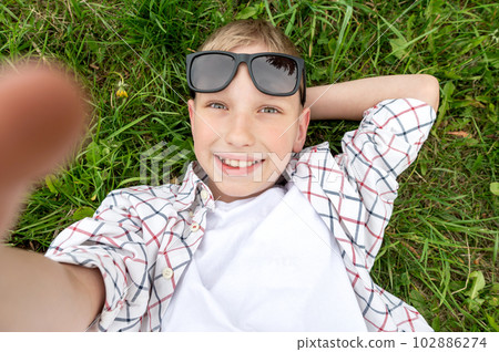 Cute boy lies in the grass with sunglasses and takes a selfie 102886274