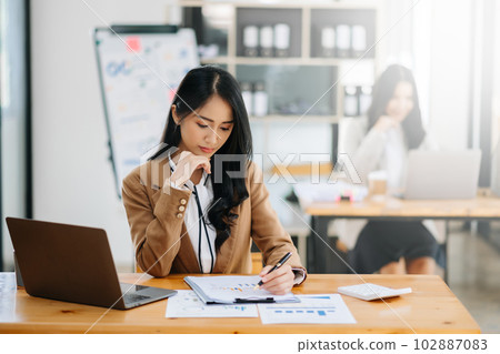 Young attractive Asian female office worker business suits smiling at camera in modern office . 102887083