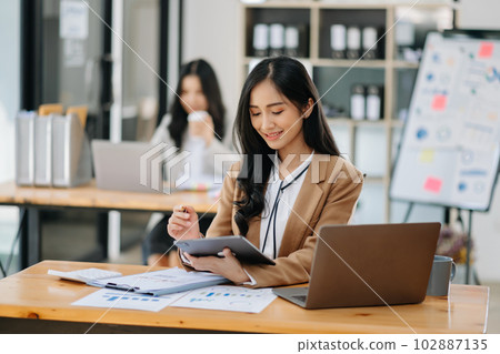 Young attractive Asian female office worker business suits smiling at camera in modern office . 102887135