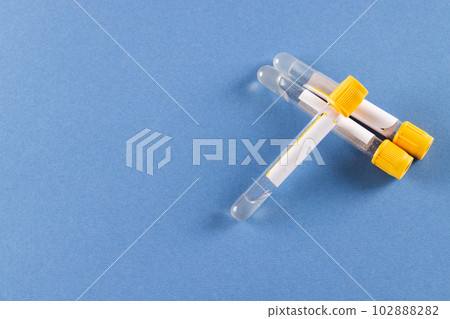 Three sample tubes of clear fluid with yellow lids, on blue background with copy space 102888282