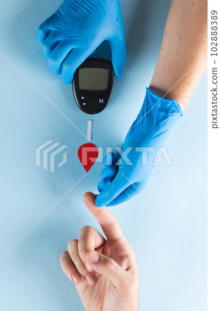 Hands of gloved doctor with glucometer taking blood sugar reading from caucasian woman 102888389