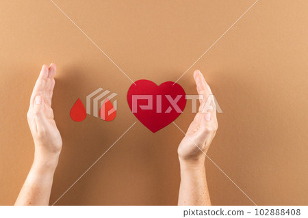 Hands of caucasian woman protecting blood drops and heart on brown background 102888408