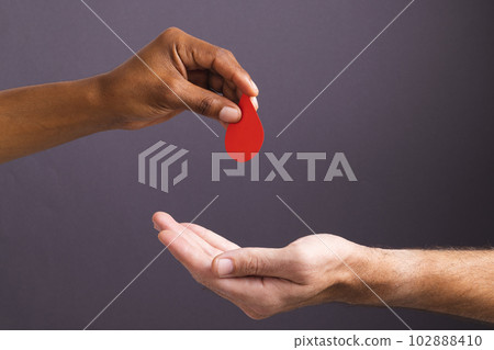 Hands of biracial man giving blood drop to caucasian man, on grey background Hands of biracial man giving blood drop to caucasian man, on grey background 102888410