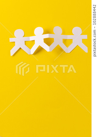 Close up of four paper cut out people figures holding hands with copy space on yellow background 102888442