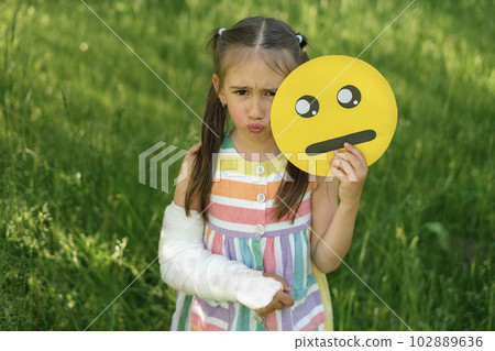 A lonely upset girl with a broken arm and a cast holds a crying emoticon 102889636