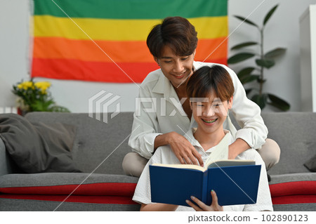 Happy moment of two young male lovers embracing each other and reading book in living room. Homosexual and love concept Happy moment of two young male lovers embracing each other and reading book in living room. Homosexual and love concept 102890123