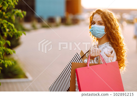 Woman in shopping. Young girl in protective sterile medical mask on her face with shopping bags. 102891215