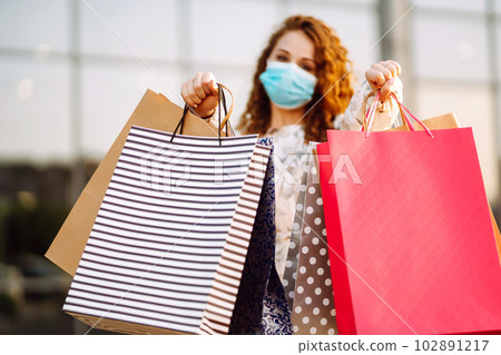Woman in shopping. Young girl in protective sterile medical mask on her face with shopping bags. 102891217