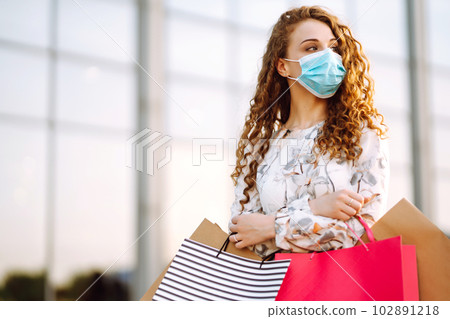 Woman in shopping. Young girl in protective sterile medical mask on her face with shopping bags. Woman in shopping. Young girl in protective sterile medical mask on her face with shopping bags. 102891218