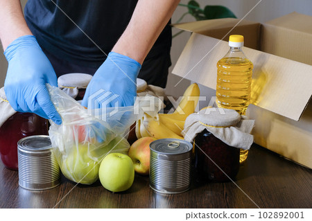 The hands of a volunteer in protective gloves are packing food into a box 102892001