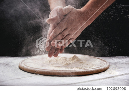 A male chef claps his hands filled with white flour on a black background. 102892008