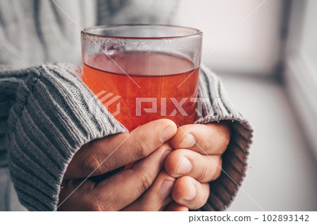 Hands in a warm white sweater are holding a mug of tea, close-up. Hands in a warm white sweater are holding a mug of tea, close-up. 102893142