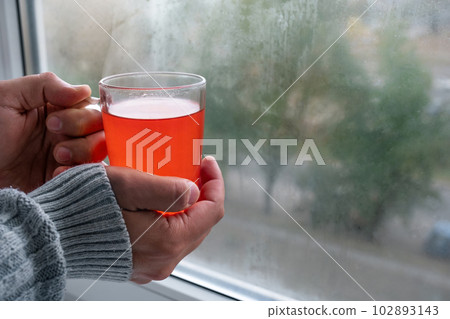 A cup of hot tea in the hands of an adult near the window A cup of hot tea in the hands of an adult near the window 102893143