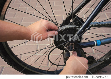 Rear wheel of a bicycle and male hands on a tiled road. Bicycle wheel repair. Rear wheel of a bicycle and male hands on a tiled road. Bicycle wheel repair. 102893248