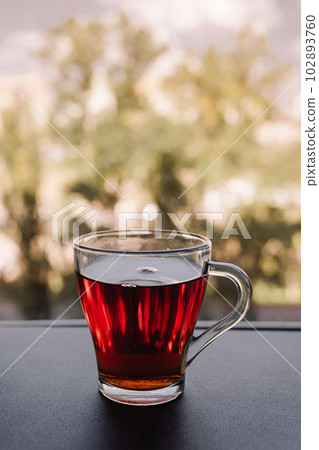 A cup of fragrant tea stands near the window. Transparent mug with a drink 102893760