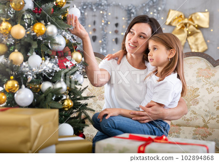 Mom and daughter holding Christmas decorations on Christmas tree 102894868
