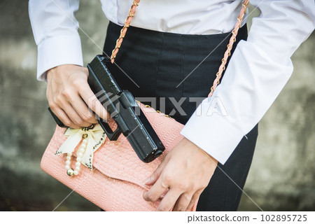 Young woman self defence putting gun in her small handbag, female hide gun in his chest, self-defense criminal concept Young woman self defence putting gun in her small handbag, female hide gun in his chest, self-defense criminal concept 102895725