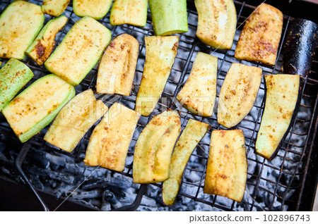 Close-up top view of zucchini slices, being marinated and cooked over flaming charcoal barbecue grill in the backyard. BBQ party. The concept of preparing food in the open air and summer chill out 102896743