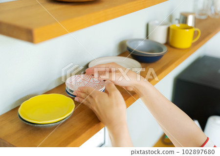 A woman's hand arranging dishes on the shelf 102897680
