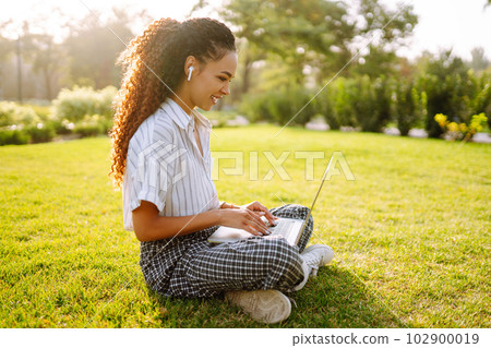 Young woman freelancer sitting on green grass with laptop. Education online. 102900019