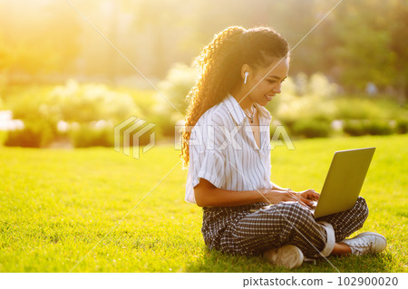 Young woman freelancer sitting on green grass with laptop. Education online. 102900020