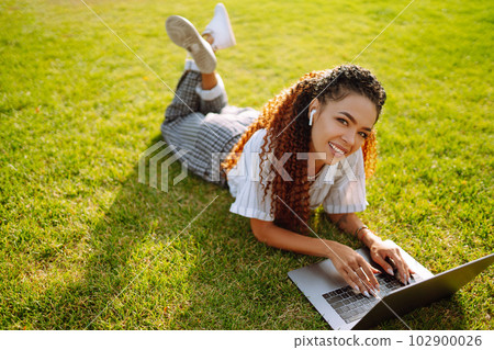 Young woman freelancer sitting on green grass with laptop. Education online. Young woman freelancer sitting on green grass with laptop. Education online. 102900026