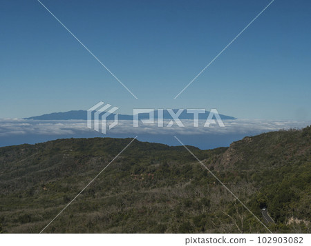 View on La Palma island seen from trail to Alto de Garajonay at Garajonay National Park. White clouds and blue sky above. La Gomera, Canary Islands, Spain, Europe. 102903082
