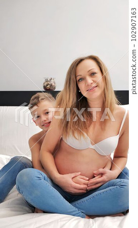 Pregnant mom talking and playing with her child in the bedroom. Mother with son sharing good emotions while relaxing at home 102907163