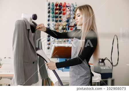 Young dressmaker standing in workshop and ironing a jacket 102908073