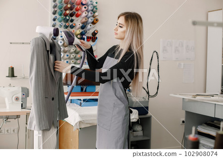 Young dressmaker standing in workshop and ironing a jacket 102908074