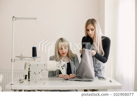 Two young seamstresses sitting on the sewing machine in her workshop 102908077