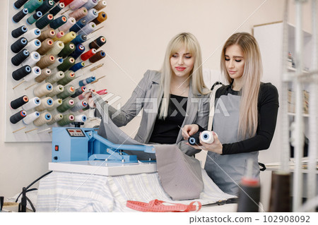 Two dressmakers standing in workshop near the bright wall with threads Two dressmakers standing in workshop near the bright wall with threads 102908092