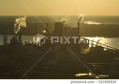 Aerial view of large factory with smokestack from production process polluting atmosphere at plant manufacturing yard. Industrial site at sunset 102908926