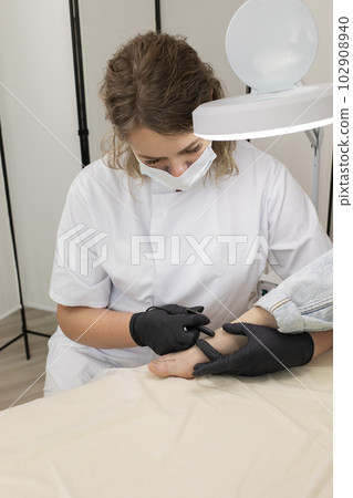 Trained Professional Remove Hair On Woman's Toes, Foot With Hair Removal Electrolysis Procedure. Electric Epilation In Beauty Salon. Vertical Plane. Authentic Photo 102908940