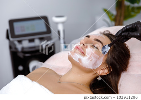 Facial treatment, Facial pampering, Cosmetic procedure, Skin purificatio, Skin scrubbing, Beauty Regimens, Dermatology Services, lifting procedure. The cosmetologist applies cream to the face of a 102911296
