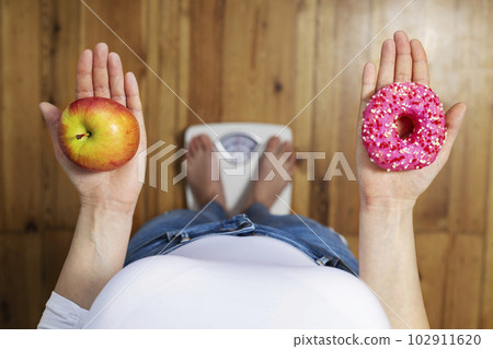 Woman measuring body weighing on weight scale, hold sweet donut and red apple 102911620
