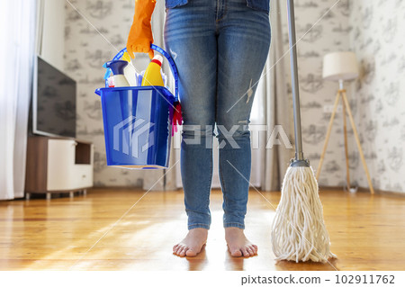 Woman in protective gloves holding a wet mop and blue bucket of detergent Woman in protective gloves holding a wet mop and blue bucket of detergent 102911762