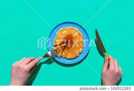 Eating pancake with maple syrup, above view. Pancake on a plate on minimalist on a green background Eating pancake with maple syrup, above view. Pancake on a plate on minimalist on a green background 102912263