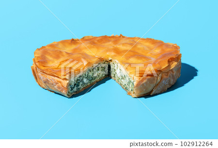 Phyllo cake with spinach and feta cheese, isolated on a blue background. 102912264