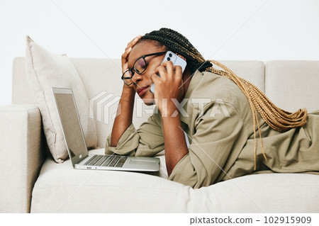 Happy african american woman business freelancer working sitting on sofa at home in laptop and phone, business calls and correspondence, light interior background. Happy african american woman business freelancer working sitting on sofa at home in laptop and phone, business calls and correspondence, light interior background. 102915909