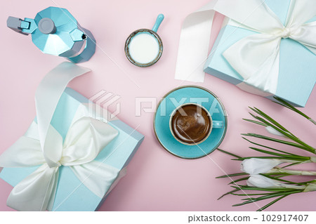 A cup of coffee and a gift box with a white bow on a pink background. 102917407
