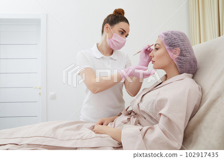 Cosmetologist drawing mark on client face to prepare for rejuvenation treatment Cosmetologist drawing mark on client face to prepare for rejuvenation treatment 102917435