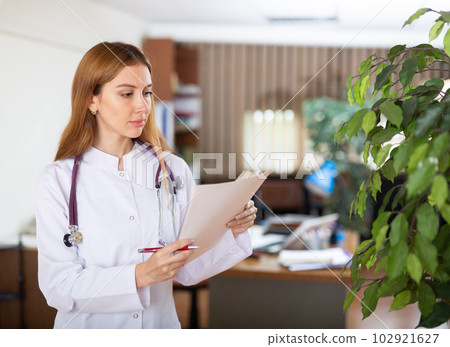 Young female therapist is studying important documents while standing in the office Young female therapist is studying important documents while standing in the office 102921627