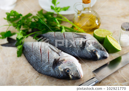 Two raw doradas served on table with herbs lime salt and oil 102921770