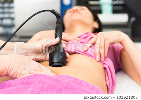 Cosmetology doctor makes a young female client a vacuum massage of the abdomen Cosmetology doctor makes a young female client a vacuum massage of the abdomen 102921808
