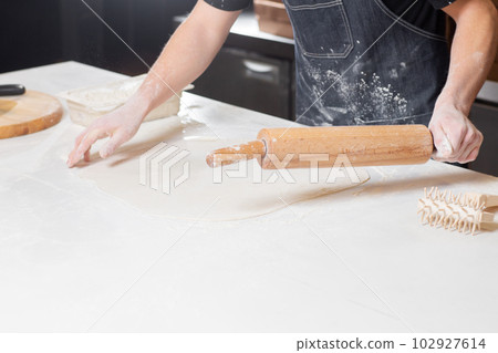 Dough for pizza, the chef rolls out the blanks. Closeup hand of chef baker in uniform white apron cook pizza at kitchen 102927614