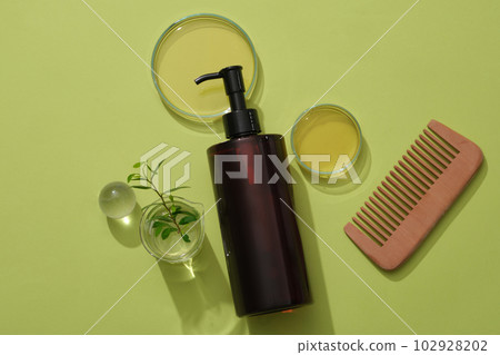 Cosmetic amber bottle unlabeled containers shampoo on green background with glassware containing essence, green leaf and comb. Mockup for design Cosmetic amber bottle unlabeled containers shampoo on green background with glassware containing essence, green leaf and comb. Mockup for design 102928202
