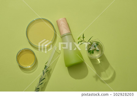 Mockup scene for advertising product with natural extract. Glass bottle unlabeled decorated with lab glassware containing essence and green leaf on green background 102928203