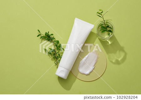 Composition of green leaves, cosmetic bottle unlabeled and cream texture on podium decorated on a green background. Minimal scene for advertising cosmetic, promote and branding 102928204