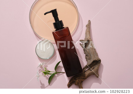 Flat lay cosmetic mockup on pink background with petri dishes containing liquid and foam, dry twig and flower branch. An amber bottle container shampoo. Advertising photo 102928223